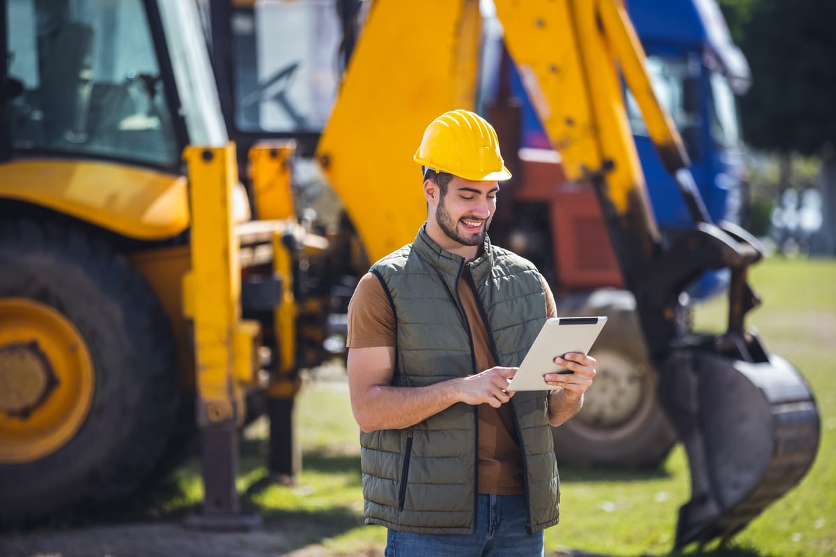 Construction worker with a tablet standing in front of an excavator